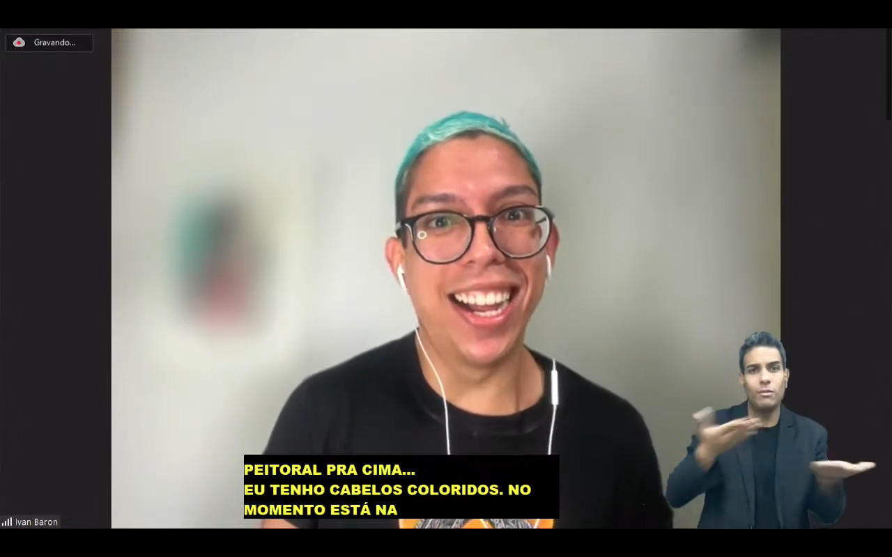 Ivan Barón é branco, usa óculos de aro grande preto e tem os cabelos pintados de azul. usa um camiseta preta. está sorrindo. 