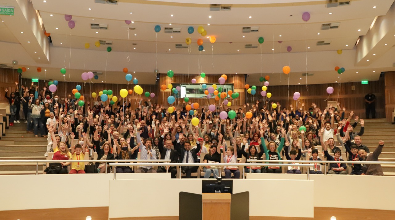 Foto do público posando para a foto sorrindo com as mãos para cima e segurando balões