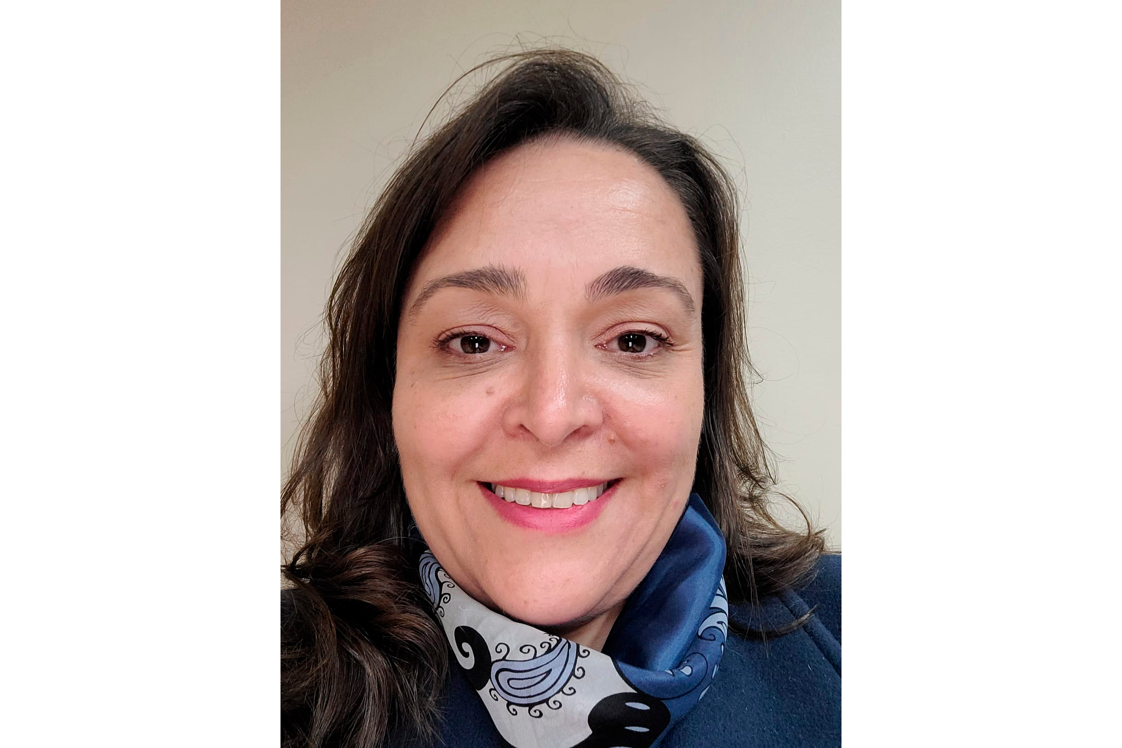 Retrato de Rejane. Ela é branca, tem o cabelo castanho, usa um casaco azul marinho e lenço em tons de azul. Está sorrindo para a foto.