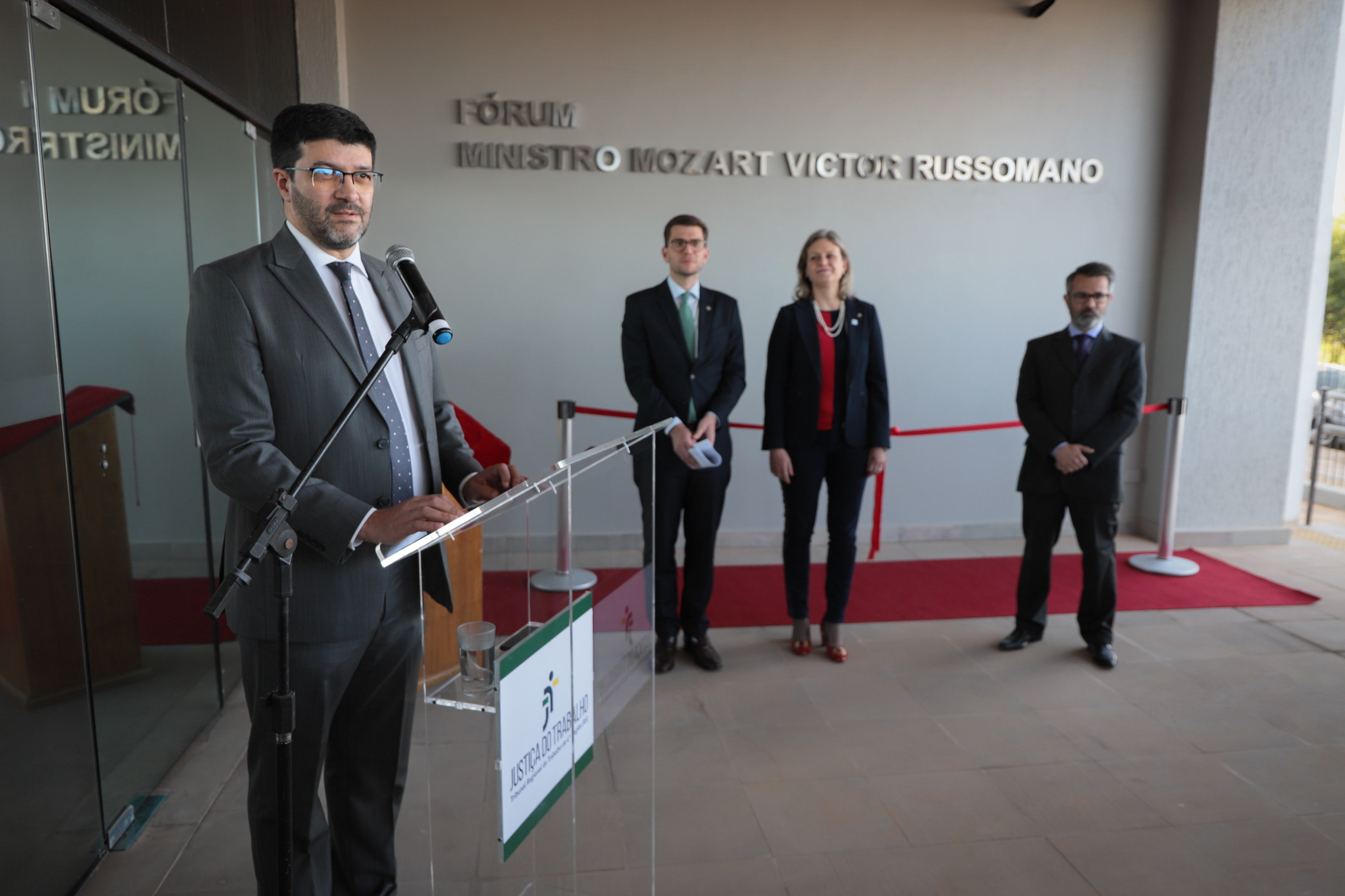 Francisco Rossal de Araújo discursa no microfone. Ao fundo aparecem as demais autoridades que falaram na cerimônia e o letreiro com o nome do ministro.