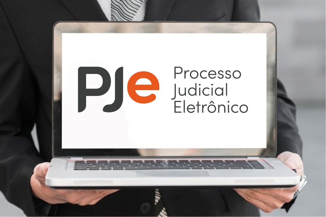 Foto de um advogado segurando um notebook com o logo do PJe na tela.