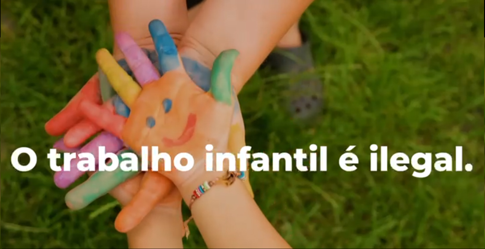 Foto de um frame do vídeo com a imagem de mãos de crianças pintadas com tinta e a frase "o trabalho infantil é ilegal"