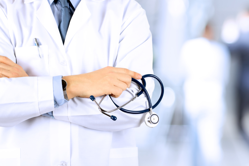Foto de um médico, vestindo jaleco branco e com um estetoscópio em volta do pescoço