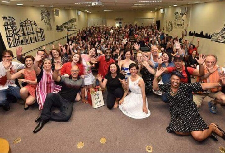 Foto do grupo de teatro com a plateia ao fundo.