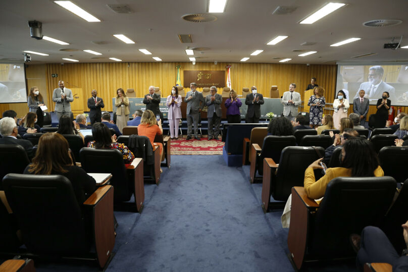 Foto do seminário, mostrando público em primeiro plano e palestrantes/autoridades em pé, em frente à mesa oficial