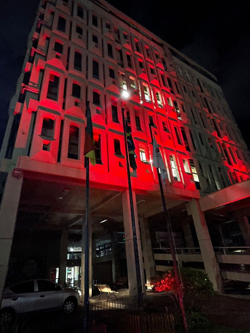 Foto da fachada do prédio da Justiça do Trabalho iluminado na cor vermelha.