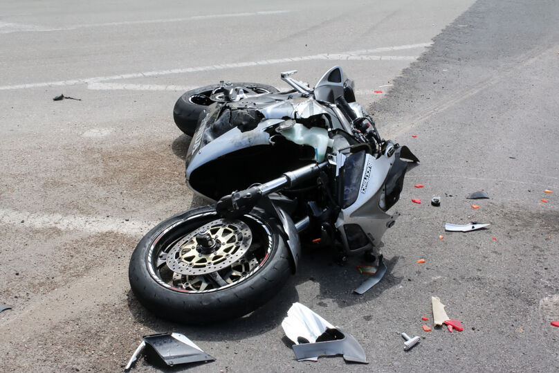 Moto na cor preta caída na estrada. Há partes do veículo quebradas. 