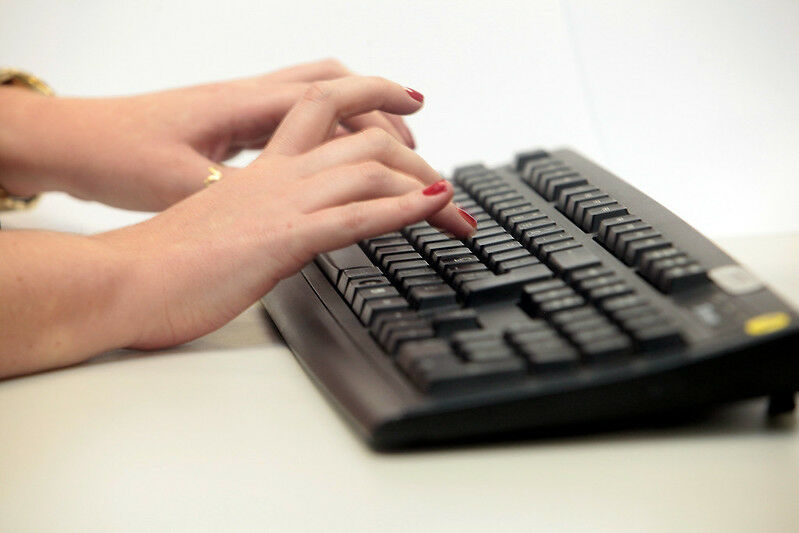 Foto de uma mulher digitando em um computador. Ângulo fechado nas mãos sobre o teclado.
