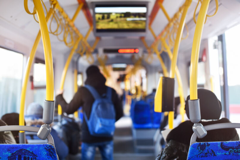 Foto mostra interior de ônibus coletivo, com passageiros sentados e outros em pé. Foto mostra interior de ônibus coletivo, com passageiros sentados e outros em pé. Predominam as cores amarela, cinza e azul.