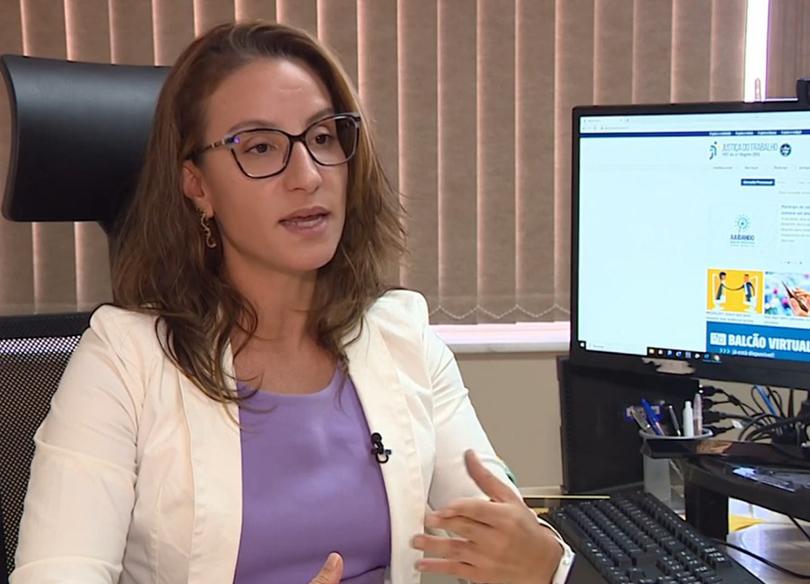 Foto da juíza Mariana Lerina falando durante a entrevista. Ela é branca, tem cabelo castanho, usa óculos de aro escuro e está gesticulando. A seu lado há um computador ligado.