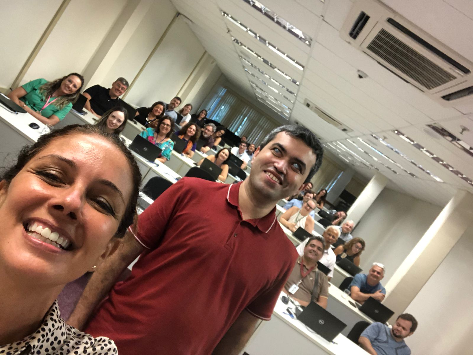 Selfie da turma. Em primeiro plano aparecem os instrutores Simone Freire e Leonardo Gleison sorrindo para a câmera. Ao fundo, aparece um grupo de cerca de 30 servidores que participou da capacitação. Eles estão nas mesas da sala de aulas da Ejud4.