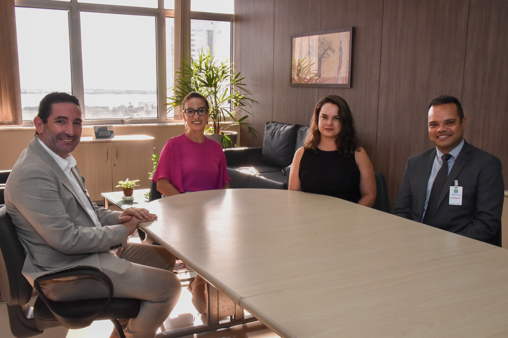 Foto dos participantes da reunião sentados ao redor de uma mesa sorrindo para a câmera.