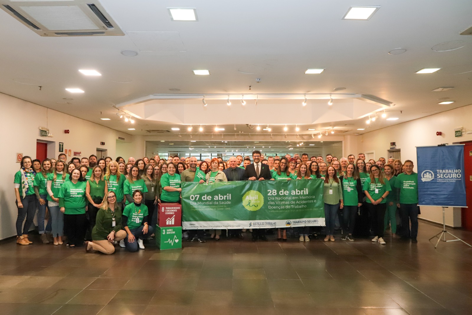 Foto de servidores e magistrados vestindo roupas verdes no saguão do prédio do TRT-4, em Porto Alegre. Na primeira fila, o presidente Francisco Rossal de Araújo e outros magistrados e servidores, seguram uma faixa alusiva ao Abril Verde.