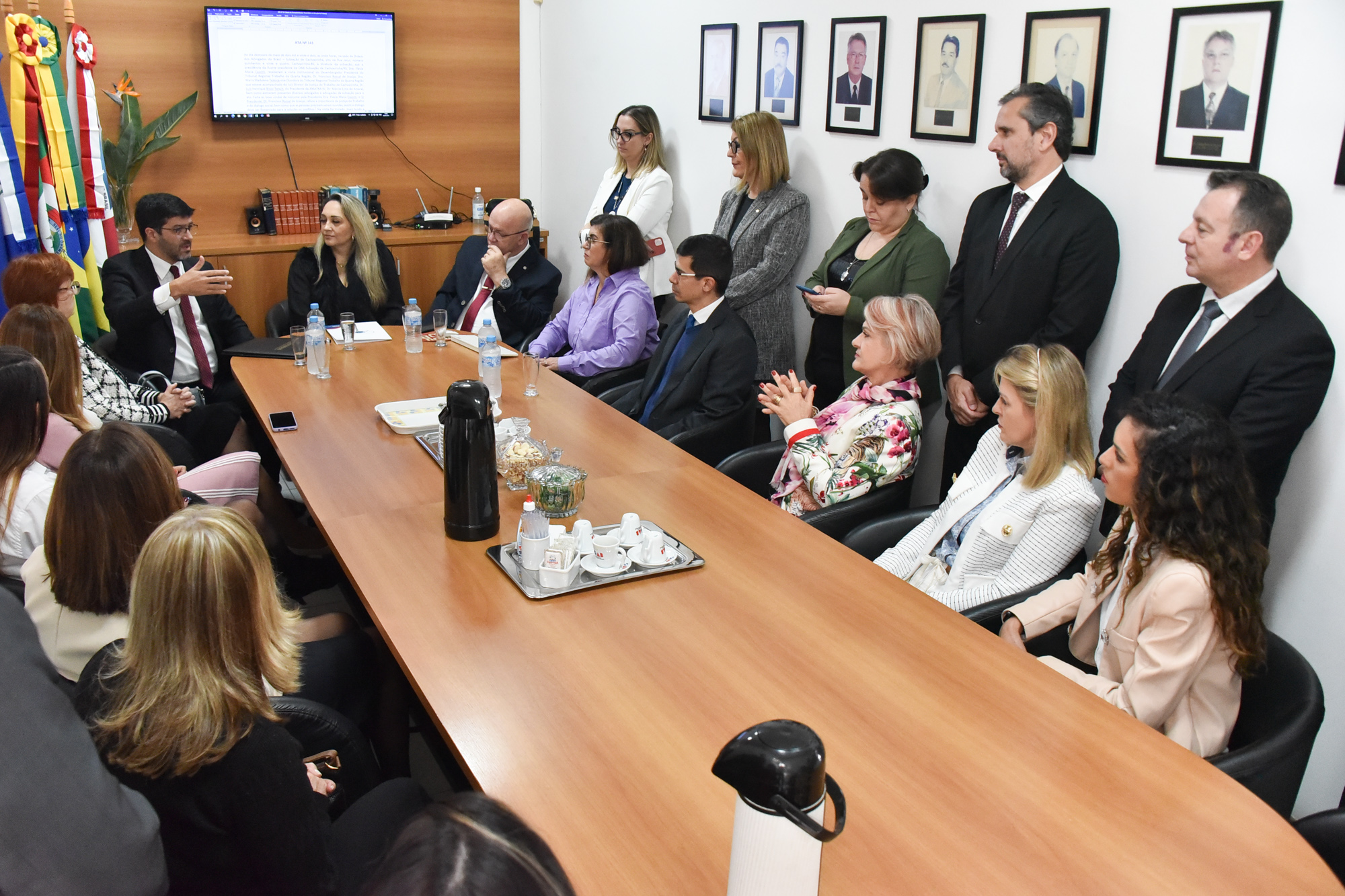 Participantes da reunião sentados e de pé em torno da mesa, na sede da OAB