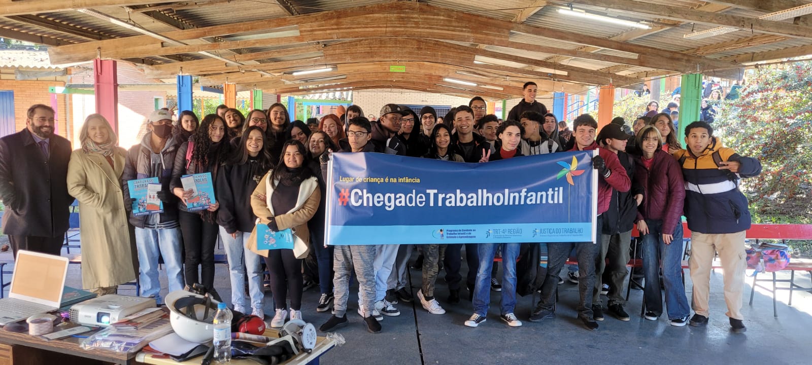 Foto de magistrados e servidores da Justiça do Trabalho gaúcha com alunos de escola de Pelotas. Uma faixa com com a frase Chega de Trabalho Infantil é segurada.