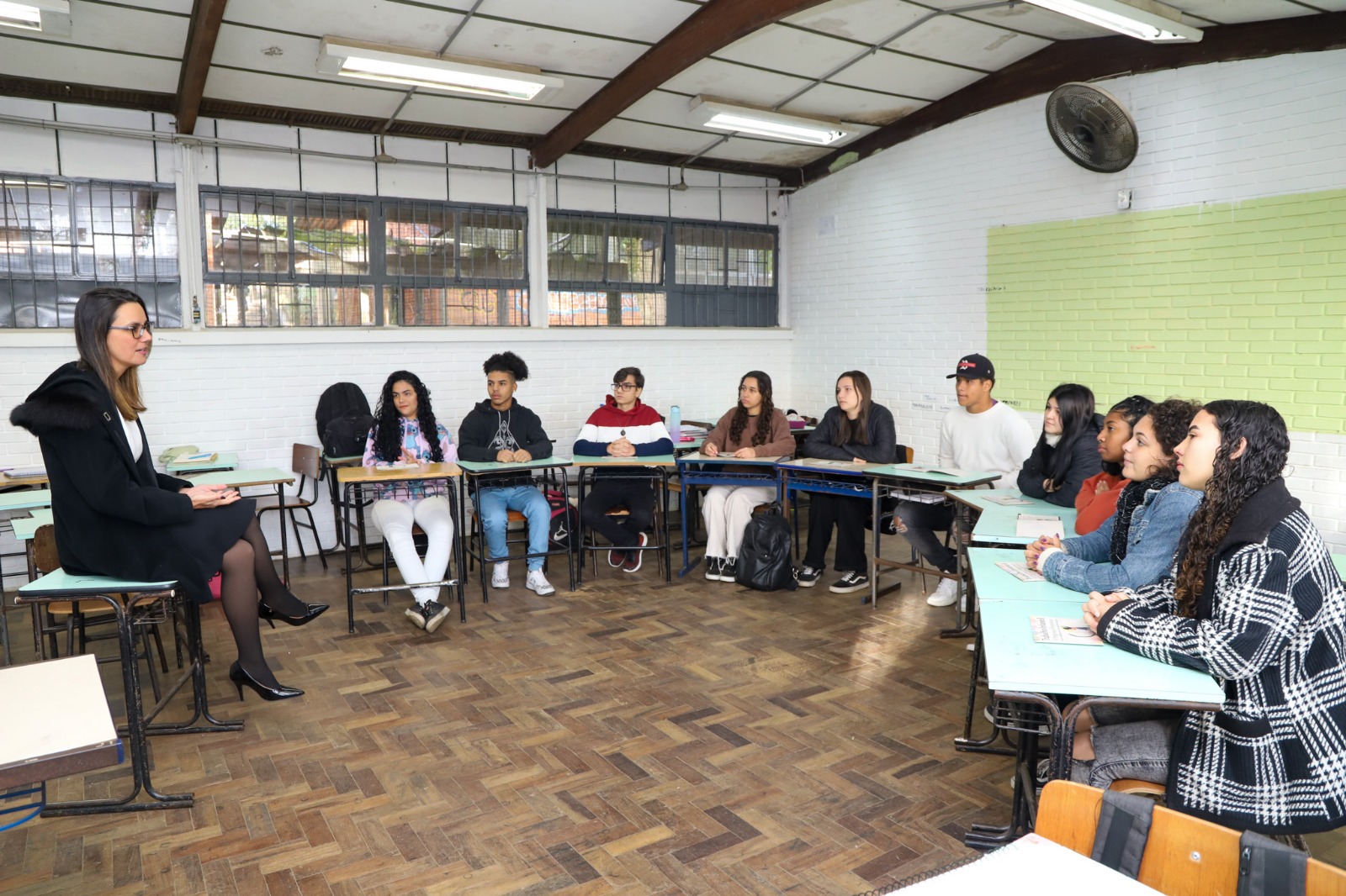 Foto de uma roda de estudantes em uma sala de aula batendo papo com a juíza Carolina Gralha sobre trabalho infantil.