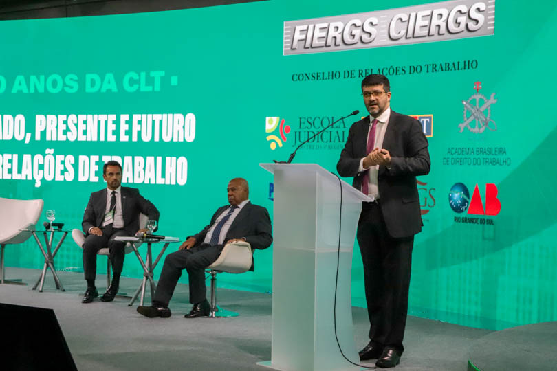 Des. Rossal falando em pé, do púlpito, com os demais participantes do painel ao fundo, sentados.
