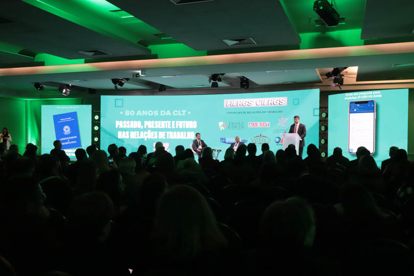 Foto em ângulo aberto do evento, mostrando palco e público.