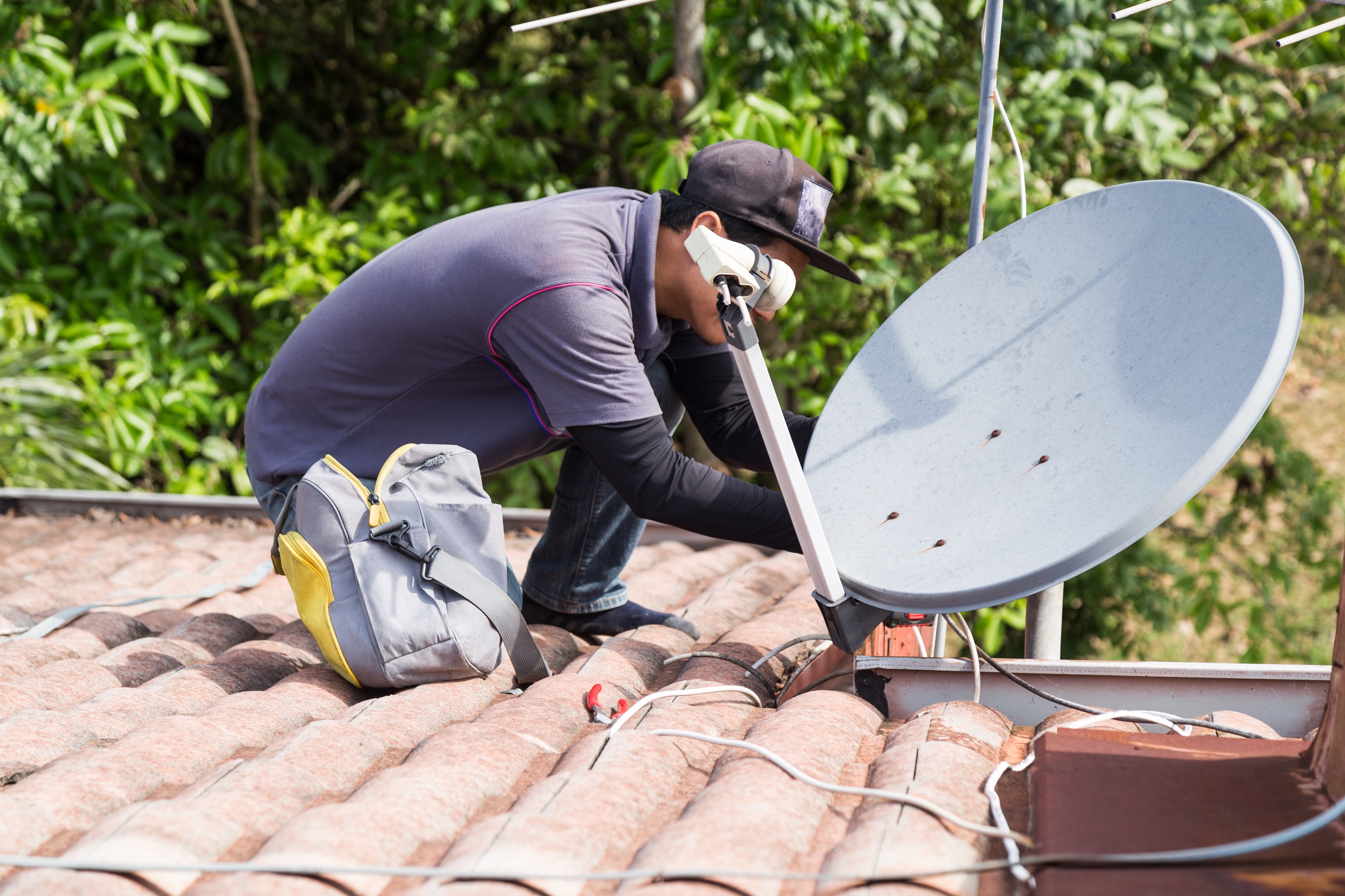 instalador de antena de tv, em cima de um telhado, com rosto encoberto pelo equipamento.