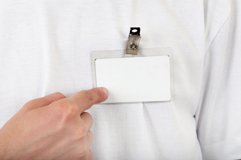 Homem aponta para crachá que está pendurado na camisa. A camisa é branca e o crachá também está em branco.