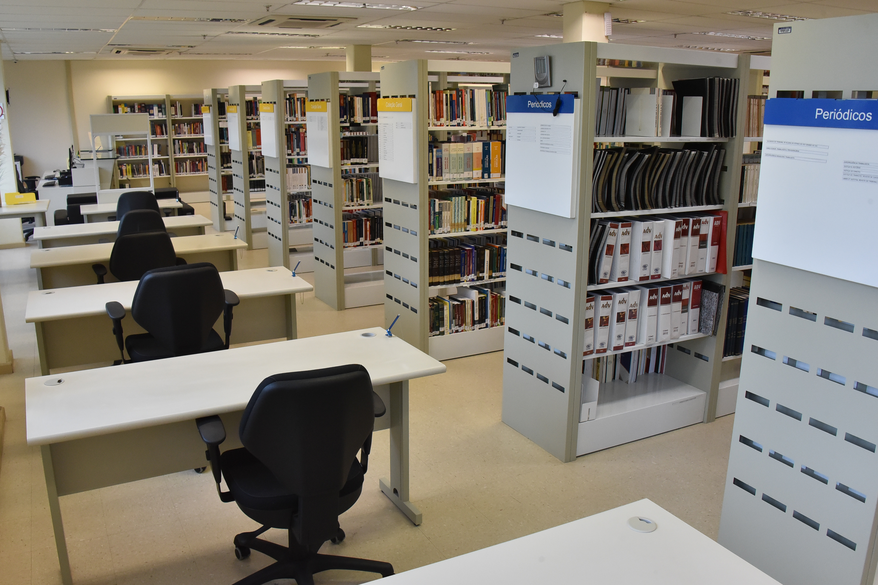 Imagem das instalações da Biblioteca do TRT-4. Há estantes com livros e mesas para estudo com cadeiras.