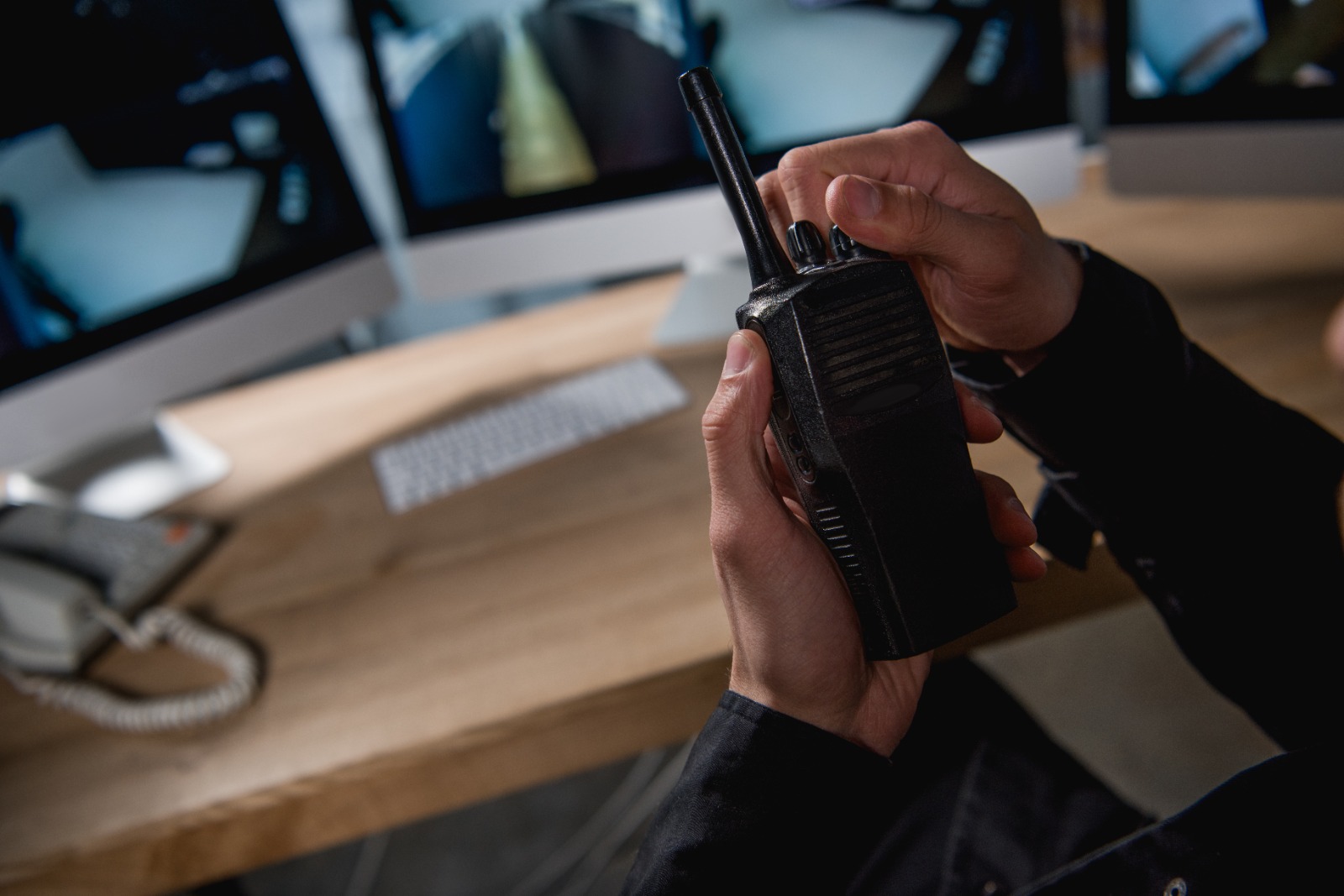 Imagem ilustrativa de um vigilante com radiocomunicador em mãos e monitorando imagens em telas