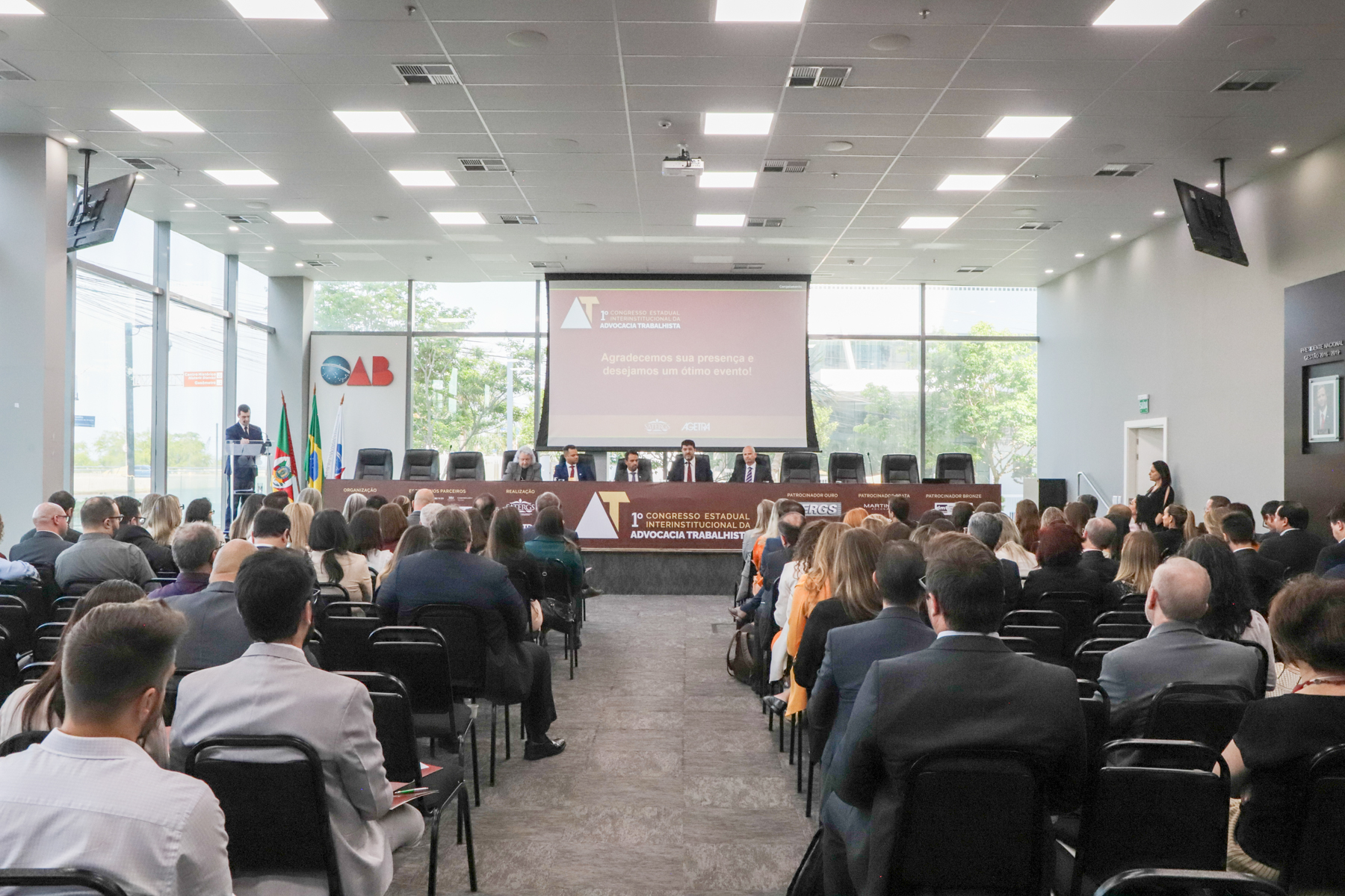 Foto em ângulo aberto, mostrando público e mesa oficial