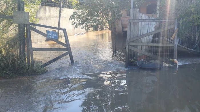 Terreno alagado, com portões de madeira abertos e casa de material ao fundo.