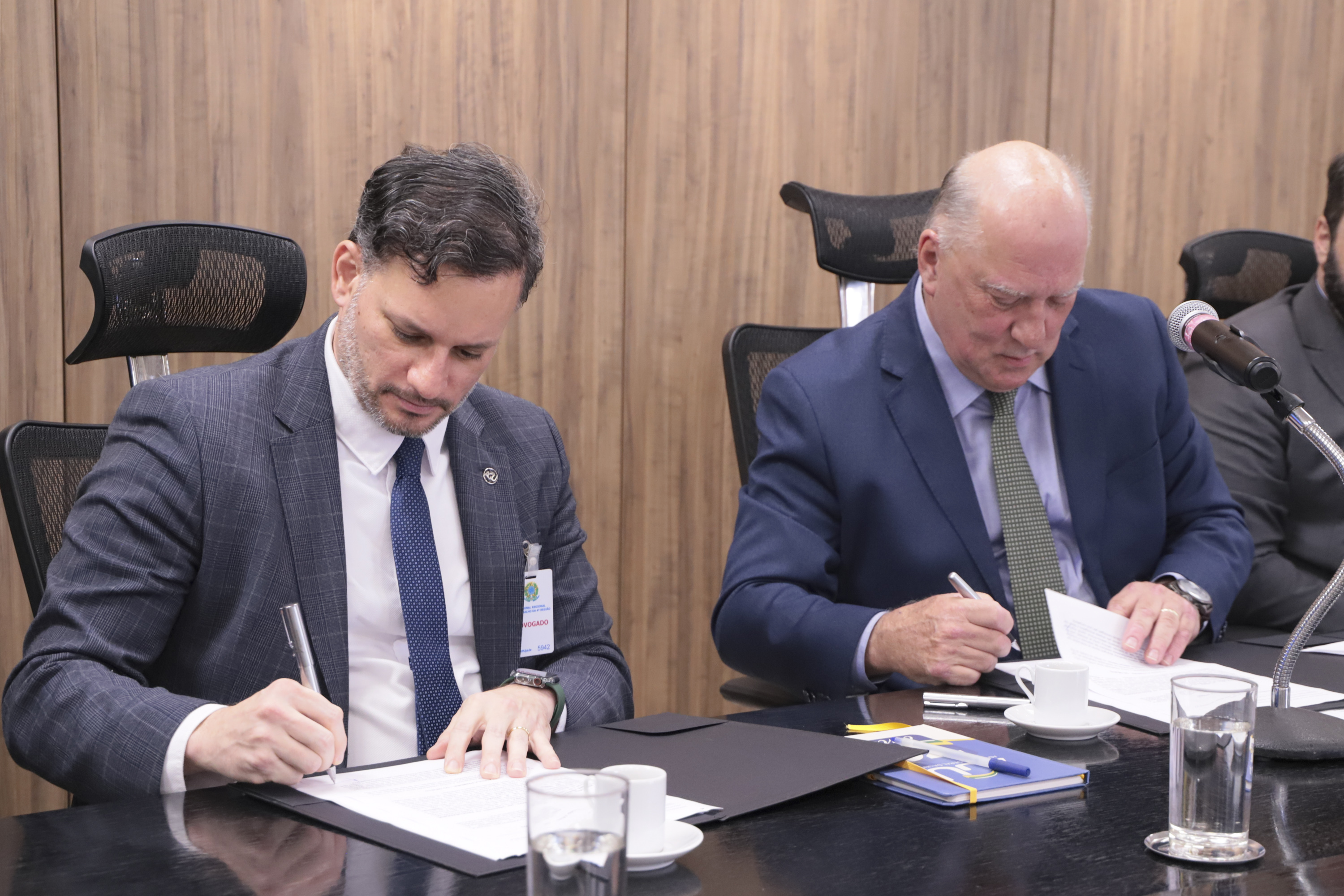 Melquizedek da Silva e Ricardo Martins Costa aparecem na mesa oficial, ambos estão assinando o acordo de cooperação