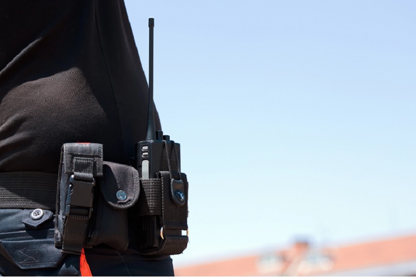 Equipamentos na cintura de vigilante. Ele veste camiseta preta e calça azul. Não há imagem do rosto.