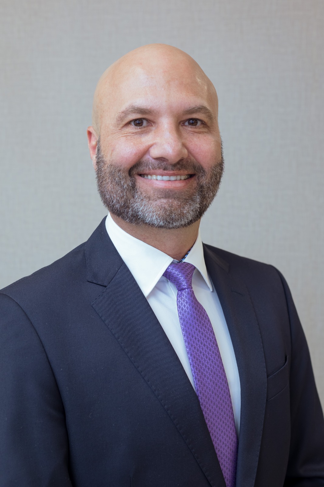 Dr. Fabiano Holz Beserra é um homem de pele clara, calvo e com a barba grisalha. Ele está sorrindo. Usa terno azul marinho, gravata lilás e camisa branca.