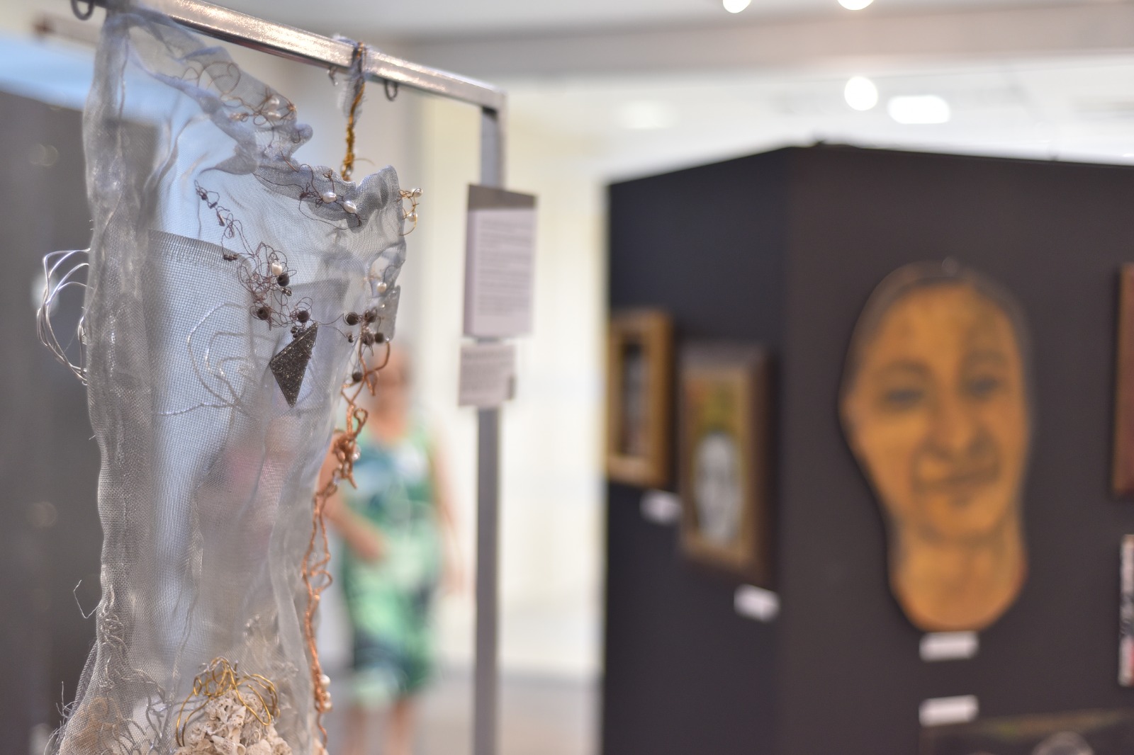 Foto em plano fechado de uma escultura em forma de corselete, feita com fio metálico prateado e materiais brilhantes