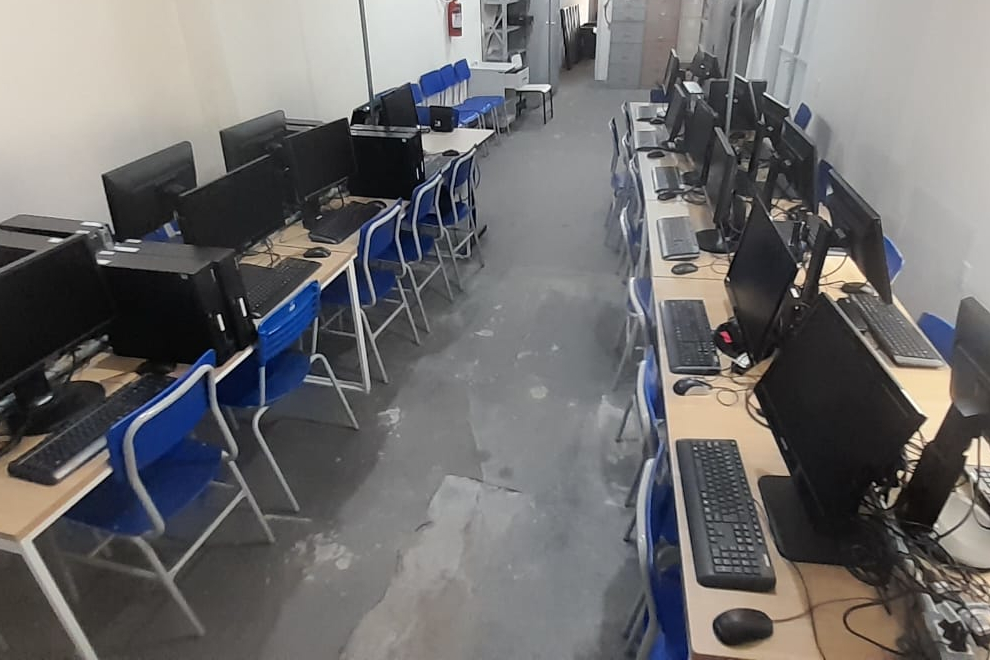 Foto da sala de informática vazia, com diversos computadores de mesa instalados lado lado.