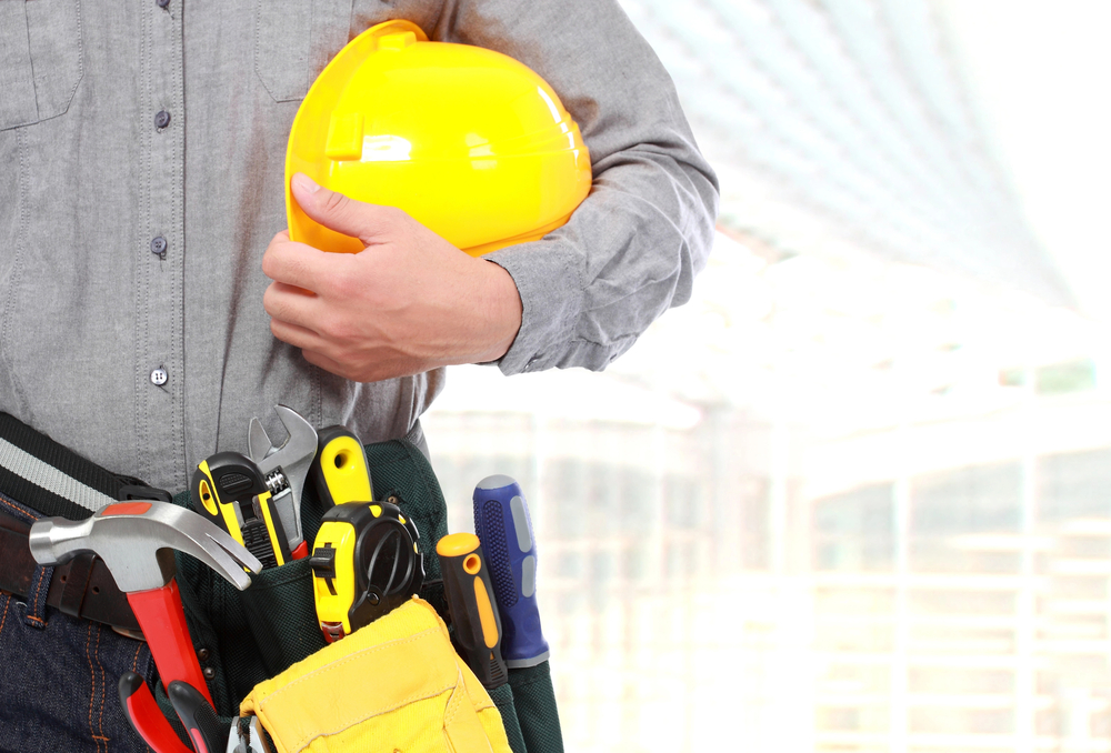 Foto ilustrativa de homem que segura capacete de obra e ferramentas.