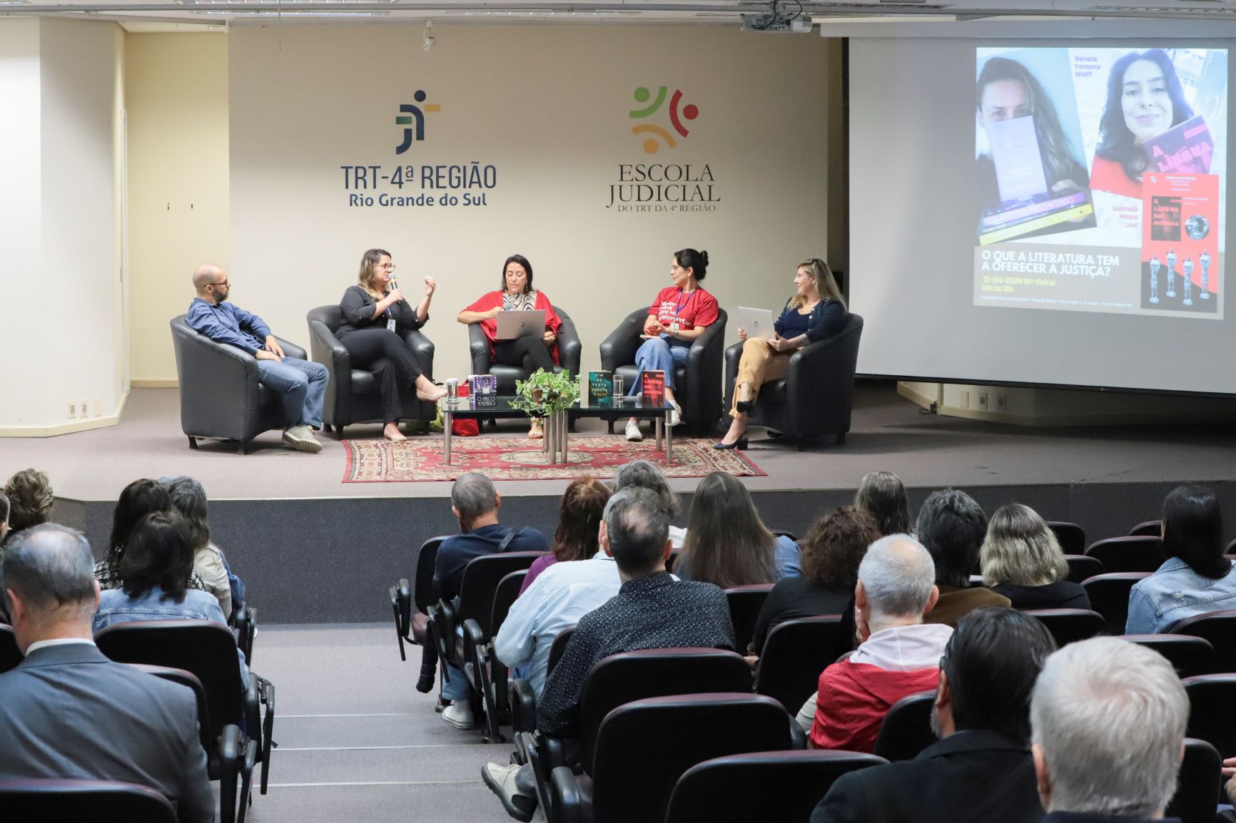 Foto das escritoras e dos mediadores no palco, com o público em primeiro plano