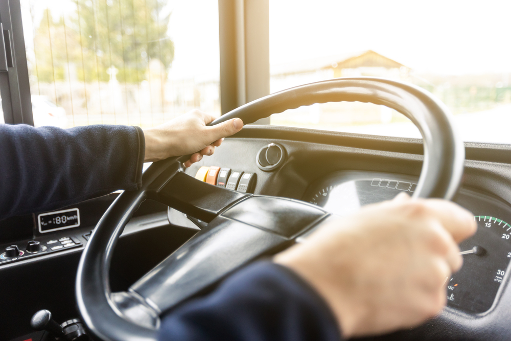 Foto em ângulo fechado de um motorista, com as mãos no volante de um ônibus.