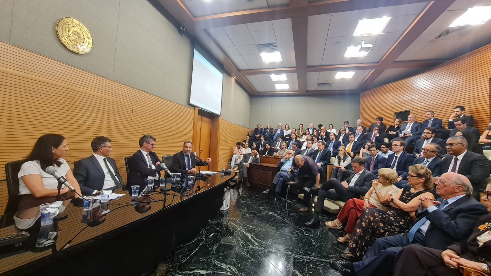 Foto do simpósio na USP, mostrando mesa e público