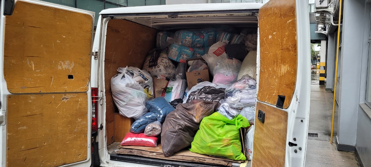 Foto de um furgão com as portas traseiras abertas, dentro vários sacos com doações distintas.