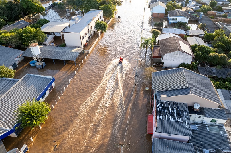 Foto aérea de cidade inundada. Há um jetski em uma rua.