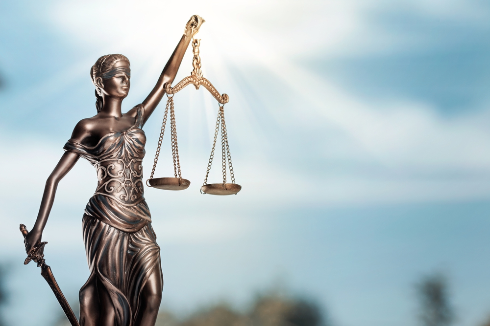 Foto de estatueta da deusa Themis. Ao fundo, céu azul.