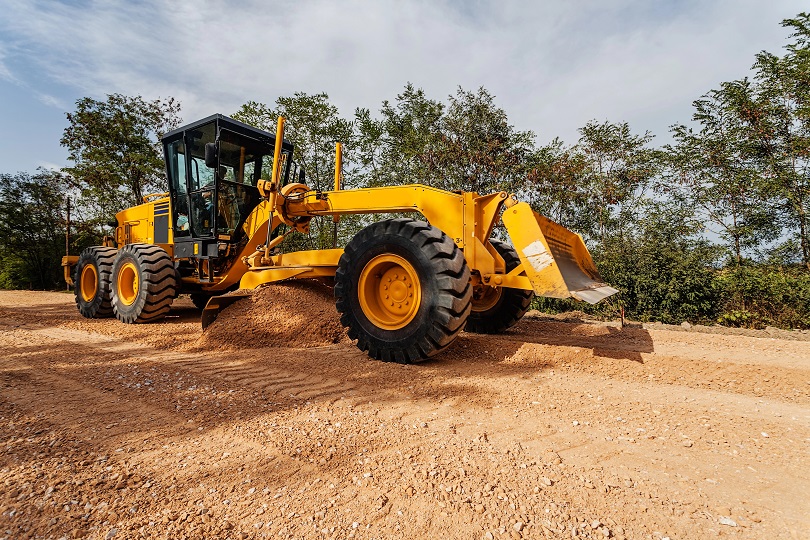 Motoniveladora em obra de construção de estrada. Máquina tem a cor amarela.