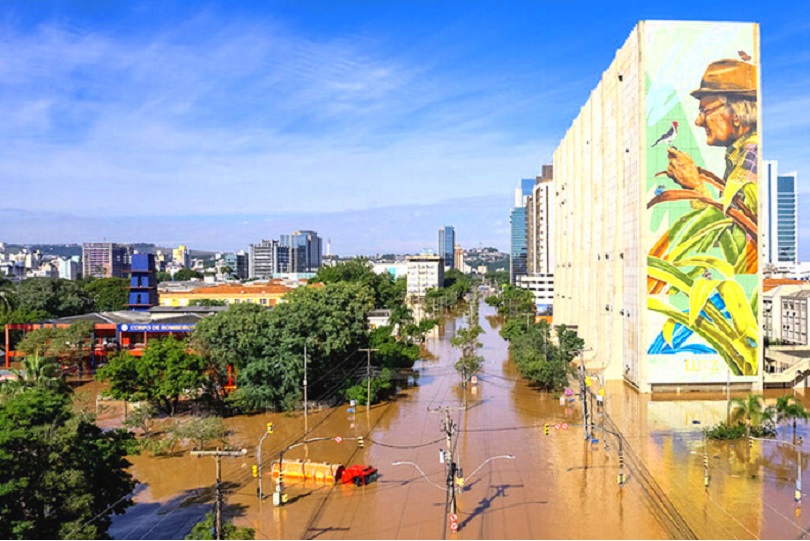 Vista parcial da cidade de Porto Alegre inundada pela água do Guaíba. À direita, há o prédio do Instituto de Previdência do Estado, com a pintura do ambientalista gaúcho José Lutzenberger. Ele está de lado, segurando um pequeno pássaro.
