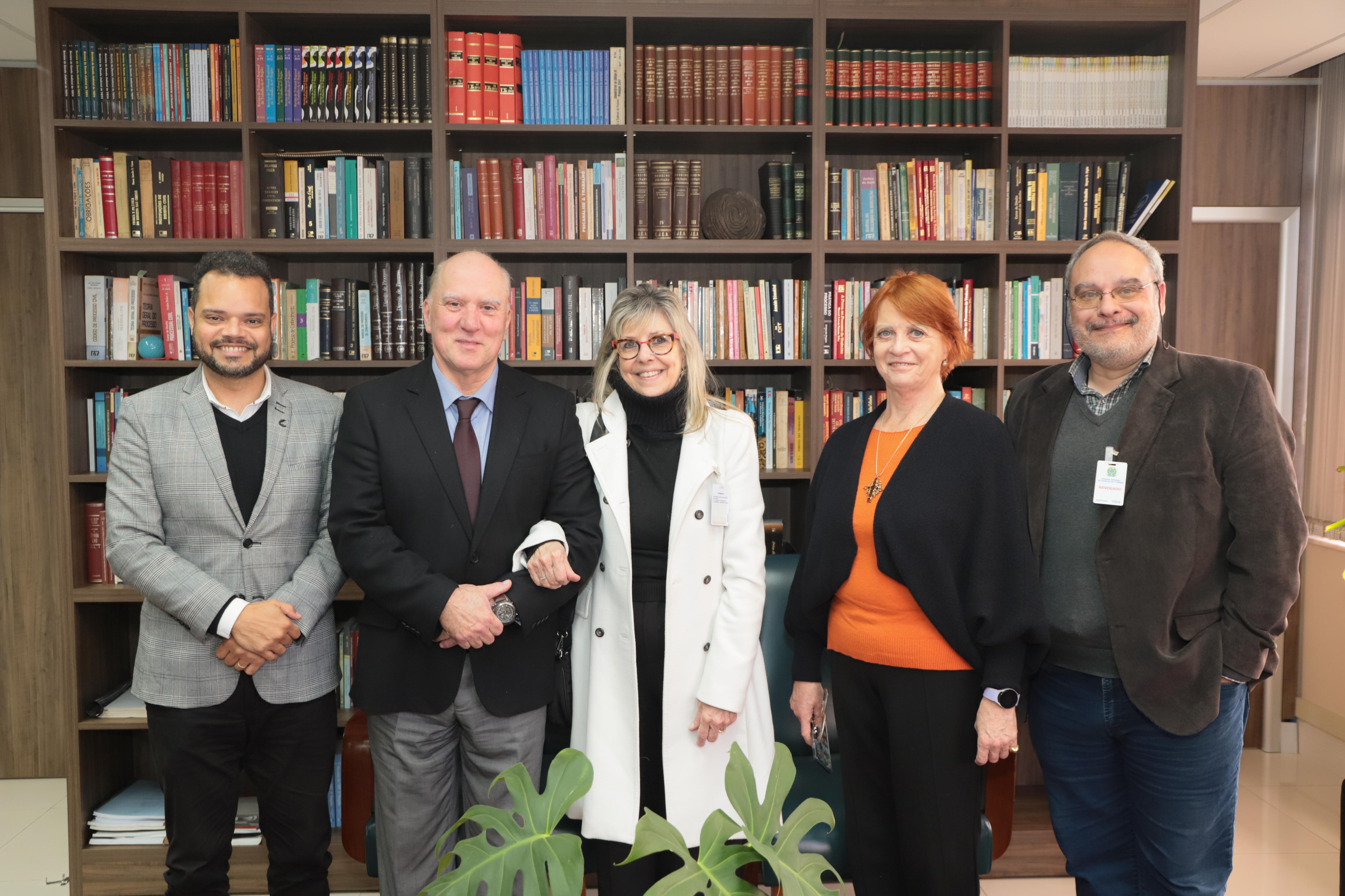 Fotos dos participantes frente a uma prateleira que vai até o teto. A prateleira está repleta de livros. Da esquerda para direita estão Saulo, Martins Costa, Sheila, Madalena e João Antonio