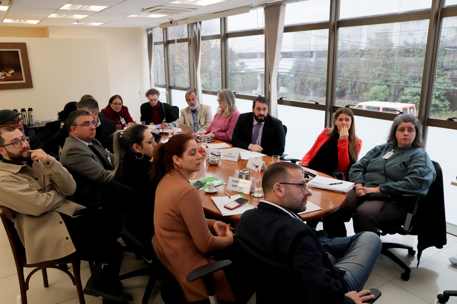 Foto durante a mediação. Os representantes das diversas instituições que participaram da mediação aparecem sentados em volta de uma mesa na sala de convivência do TRT-4
