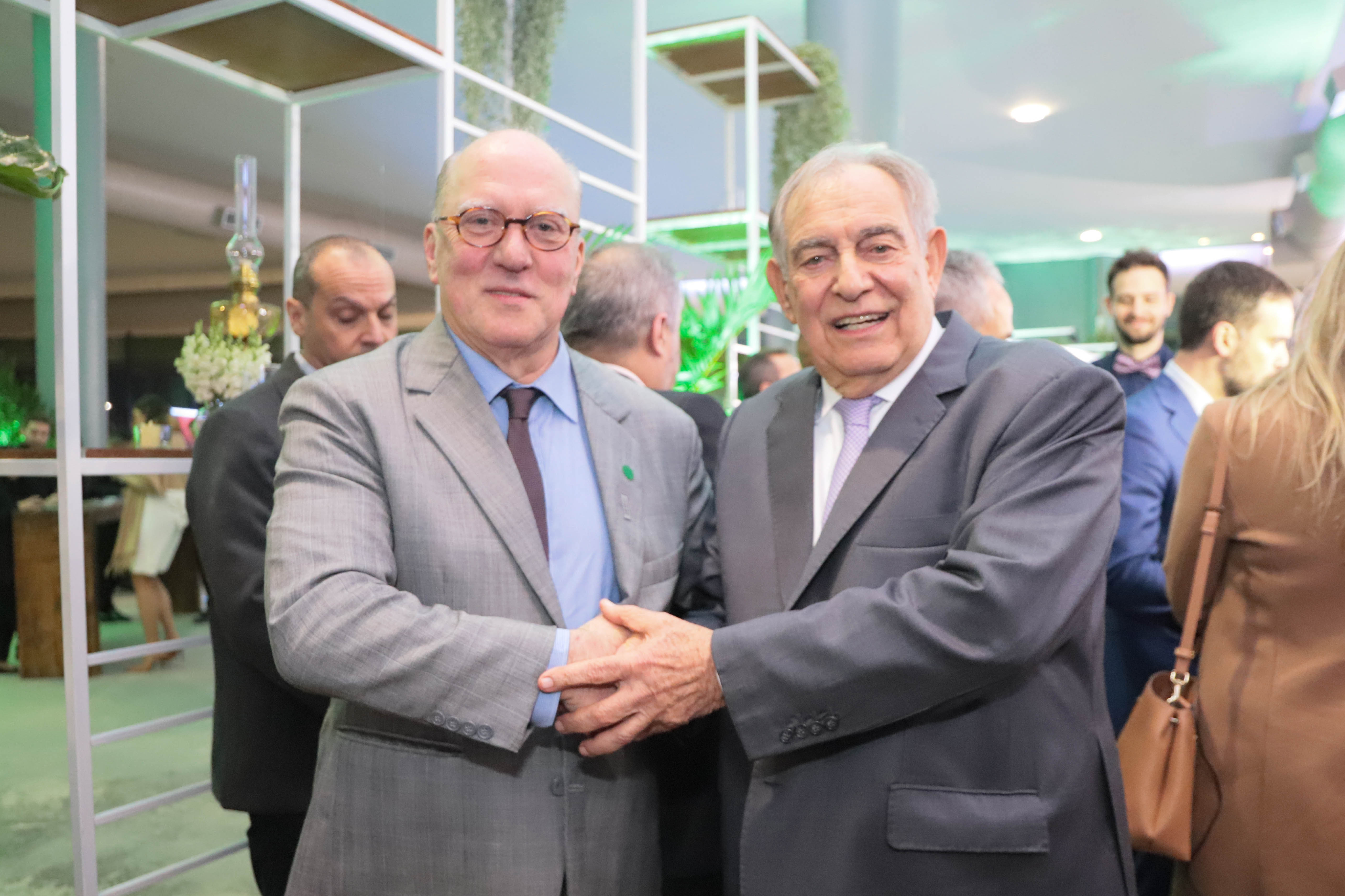 Ricardo Martins Costa e Cláudio Bier posam para a foto antes do evento. Eles sorriem para a câmera e se apertam as mãos.