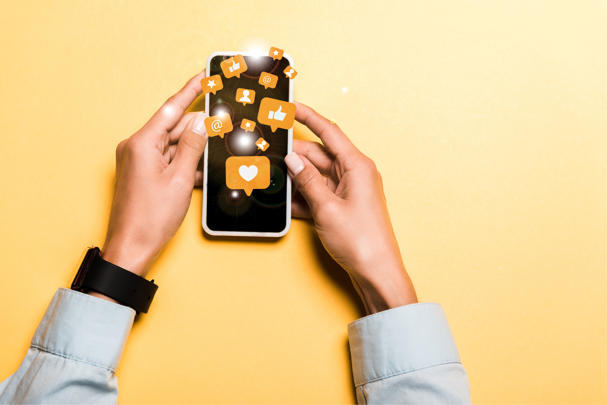 foto ilustrativa das mãos de uma mulher segurando um celular. Desenhos de balões de diálogos saem da tela com símbolos de curtidas e interações nas redes.