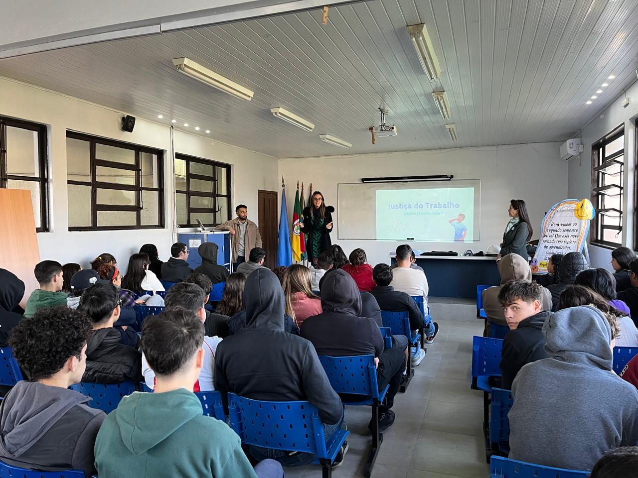 Turma de 3 ano em palestra sobre temas de discriminação do trabalho com slide no fundo