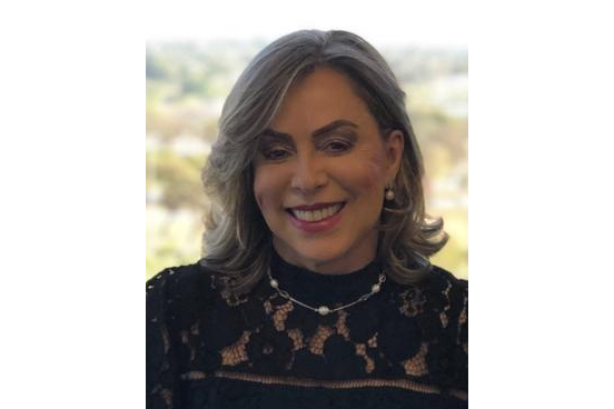 Foto da ministra Dora Maria da Costa. Ela é parda, tem cabelo liso e loiro, usa um vestido preto e está sorrindo para a câmera