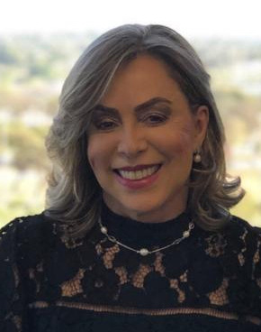 Foto da ministra Dora Maria da Costa. Ela é parda, tem cabelo liso e loiro, usa um vestido preto e está sorrindo para a câmera
