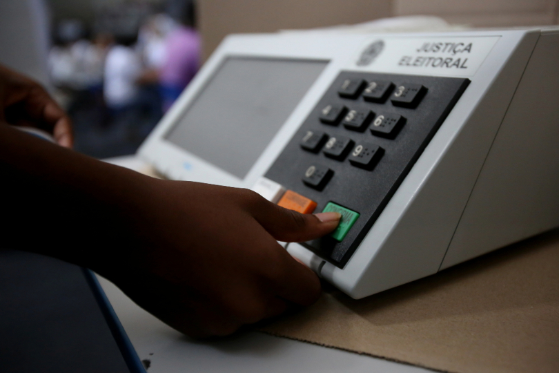 Mão feminina, de pele negra, registra voto em urna eletrônica.